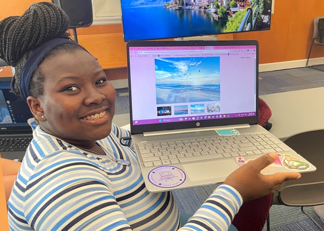 Girls Code Savannah student Gabby smiling while presenting her newly-coded interactive image gallery on a laptop